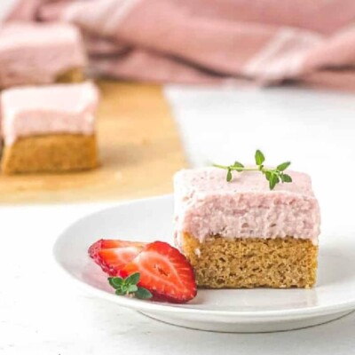 A small white, round, plate with a strawberry thyme blondie next to a fresh strawberry cut in half.