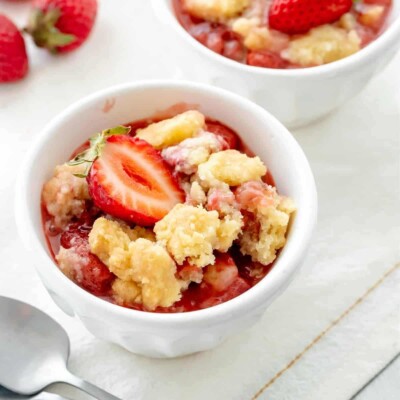 A small bowl of strawberry dump cake with a spoon and another bowl in the background.