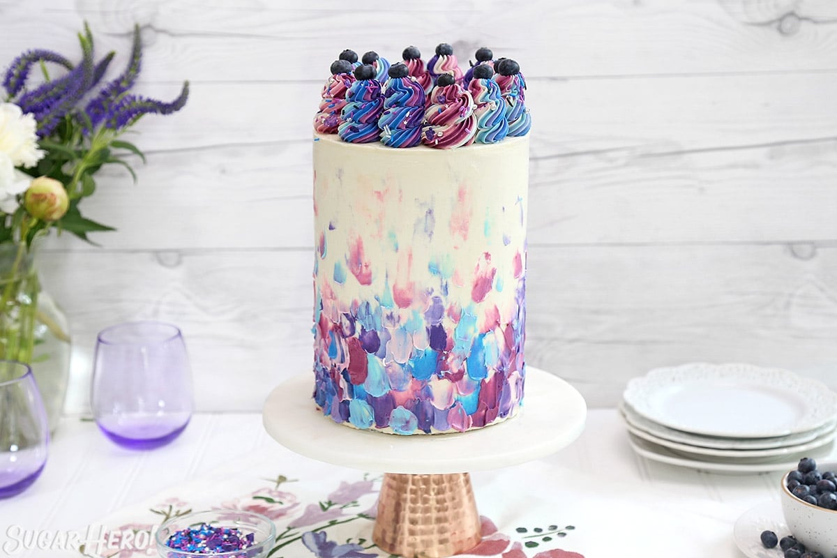Blueberry Layer Cake with blue and purple frosting on a gold-bottomed cake stand.