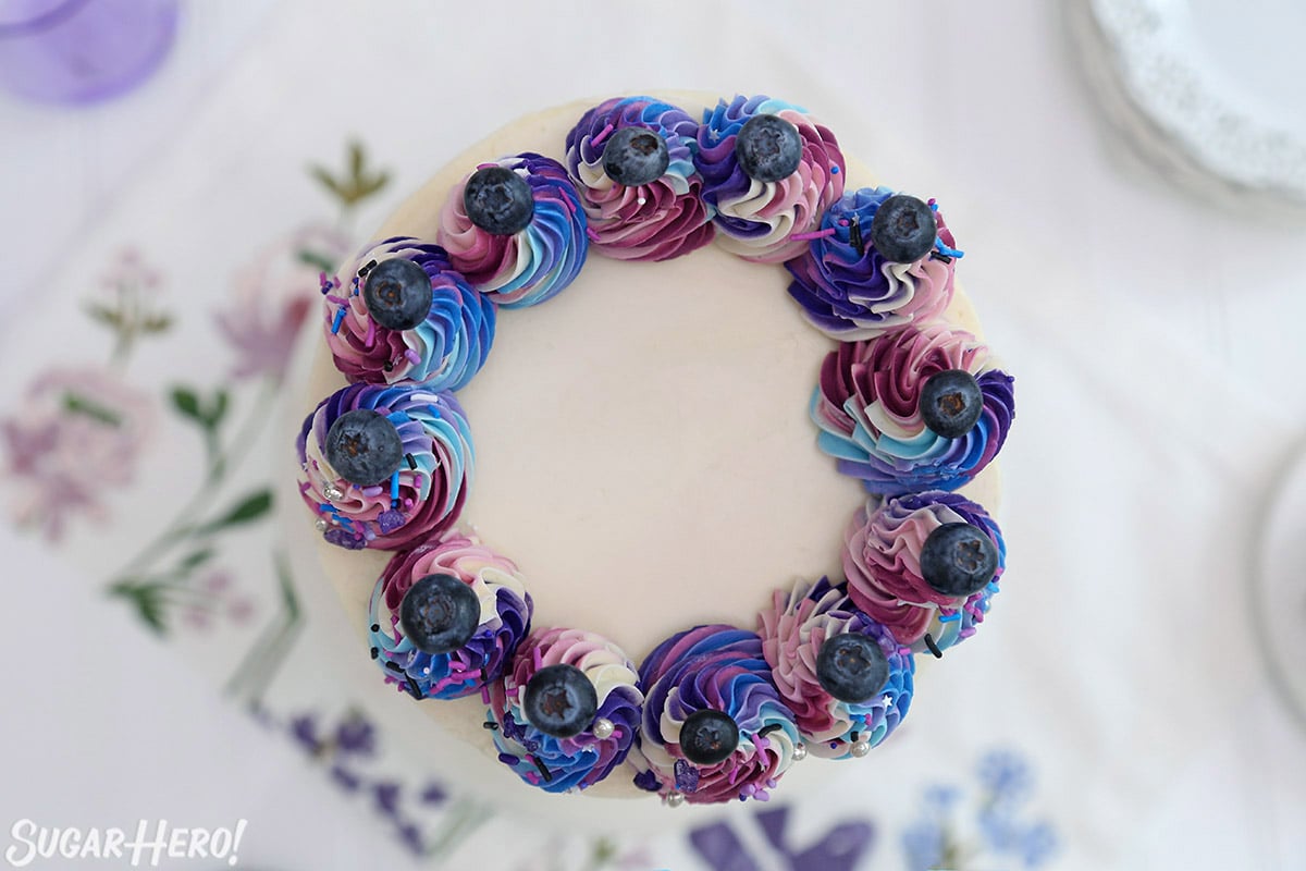 Overhead shot of multi-colored rosettes with blueberries on top on a blueberry layer cake.