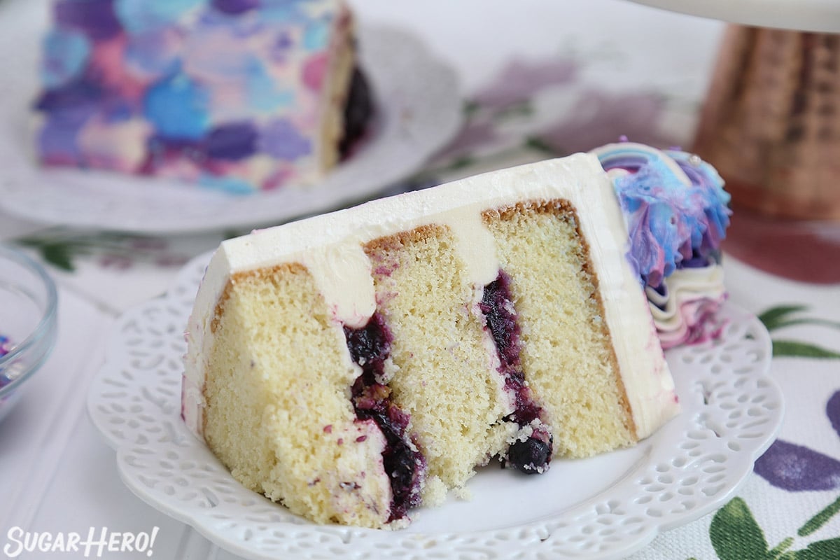 Close-up of a slice of blueberry layer cake on a white plate.