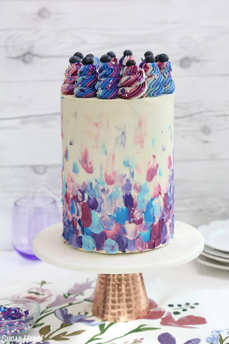 Blueberry Layer Cake with blue and purple frosting on a gold-bottomed cake stand.