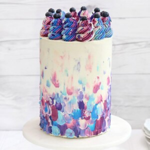 Extra-tall Blueberry Cake on a marble cake stand in front of a white wooden background.