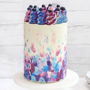 Extra-tall Blueberry Cake on a marble cake stand in front of a white wooden background.