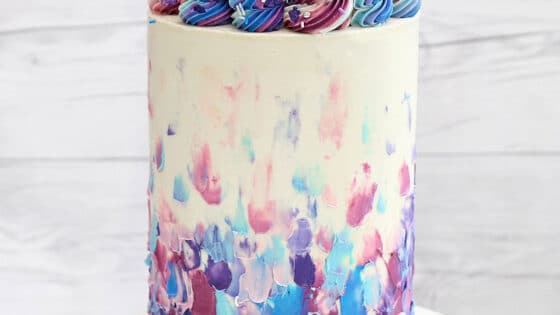 Extra-tall Blueberry Cake on a marble cake stand in front of a white wooden background.