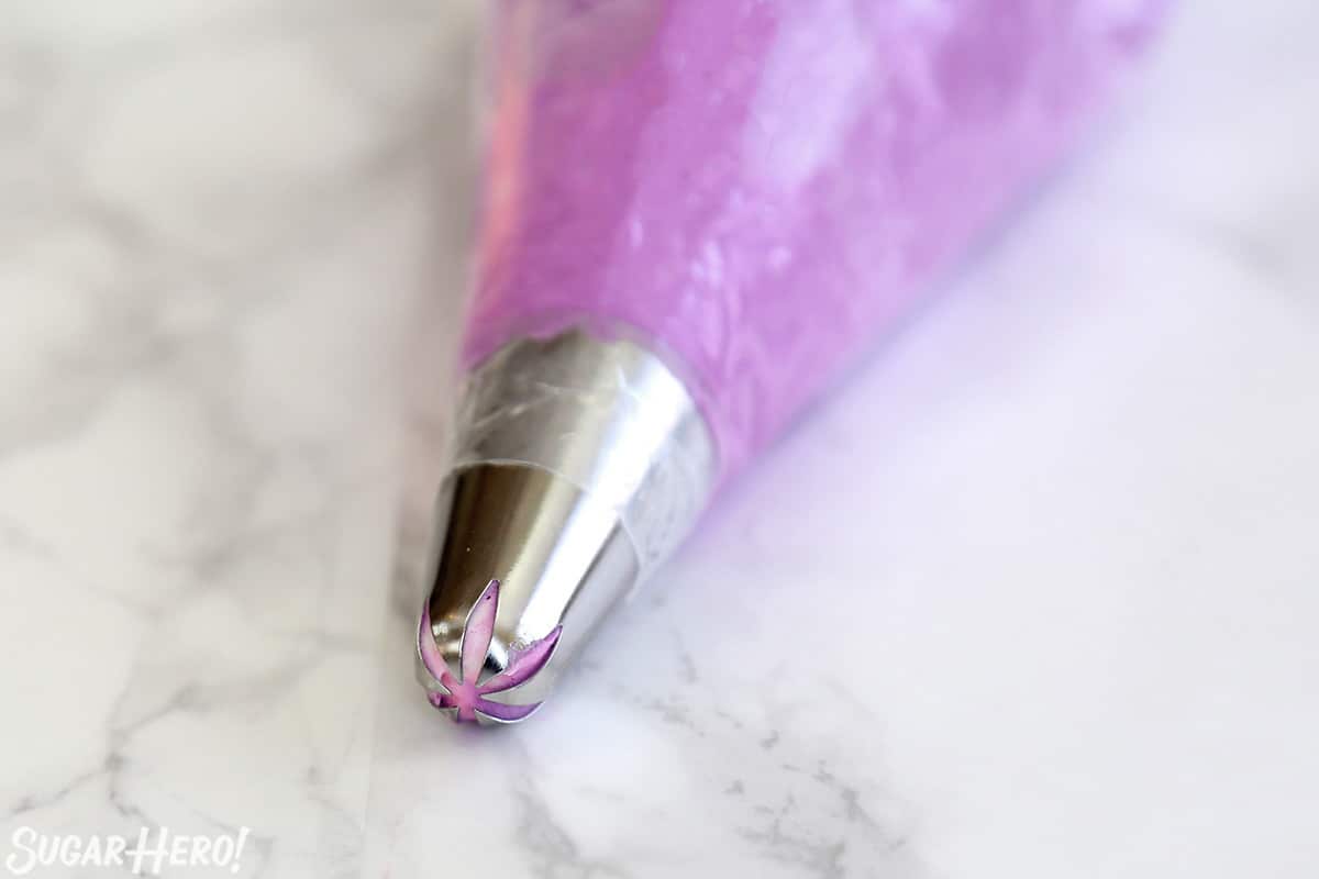 Close-up of piping bag with purple frosting fitted with a star tip.