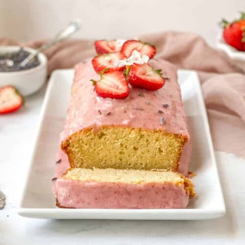 A loaf of lavender pound cake covered with strawberry glaze and fresh strawberries.