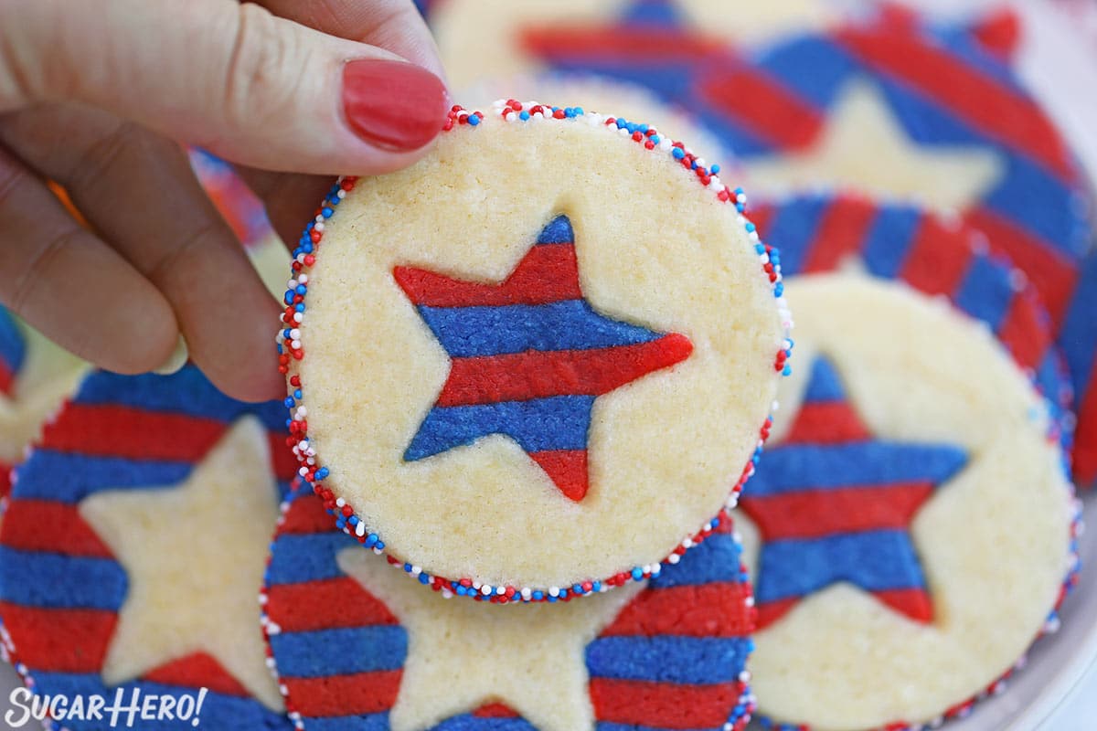 Close-up of a hand with a red nail holding a Stars and Stripes Sugar Cookie.