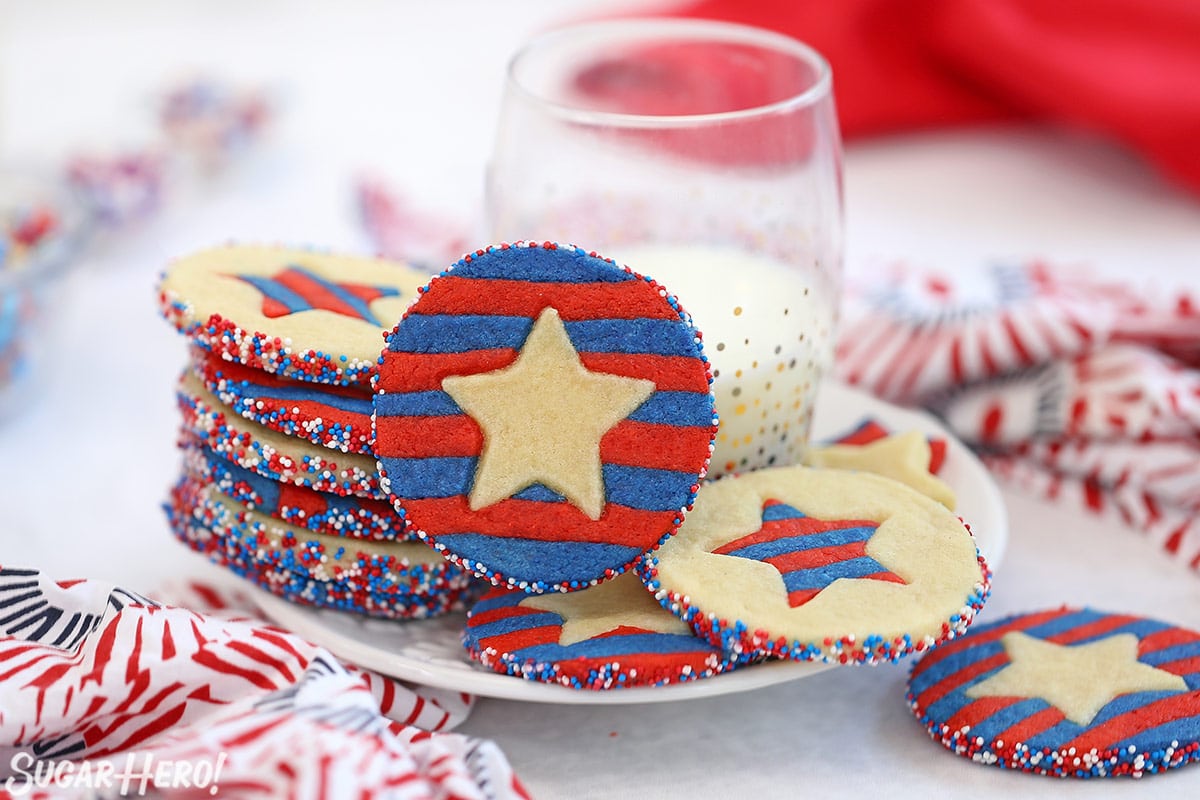 Stars and Stripes Sugar Cookies stacked on a plate and leaning against a glass of milk.
