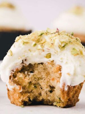Close-up of zucchini cupcake frosted with cream cheese frosting, with a big bite taken out of it.
