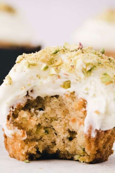 Close-up of zucchini cupcake frosted with cream cheese frosting, with a big bite taken out of it.