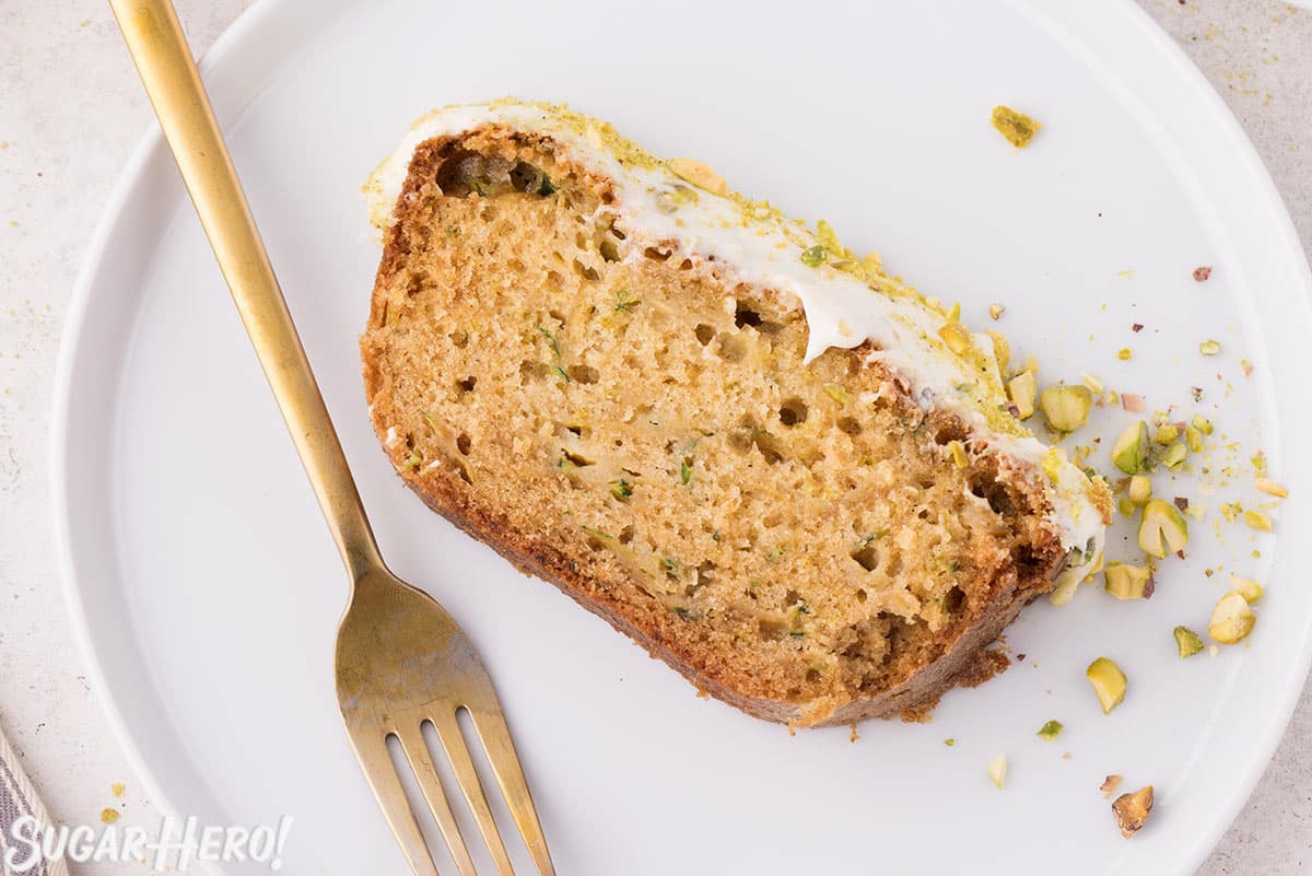 Slice of zucchini bread on a white plate with a gold fork next to it.