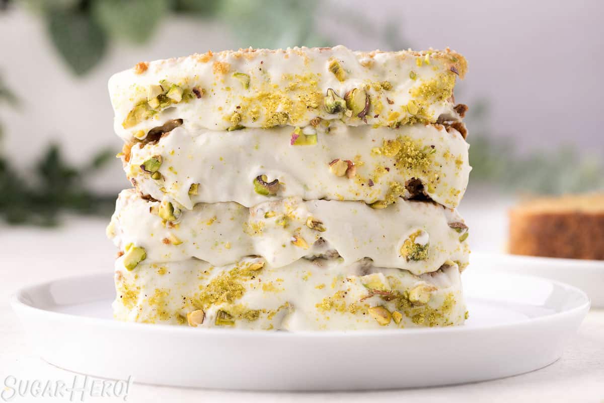 Four slices of zucchini bread on a white plate, with cream cheese frosting and crushed pistachios on top.