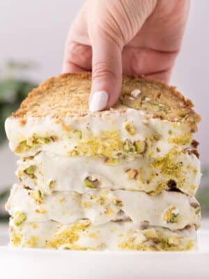 A stack of zucchini bread frosted with cream cheese frosting, with a hand lifting up the top piece of bread.