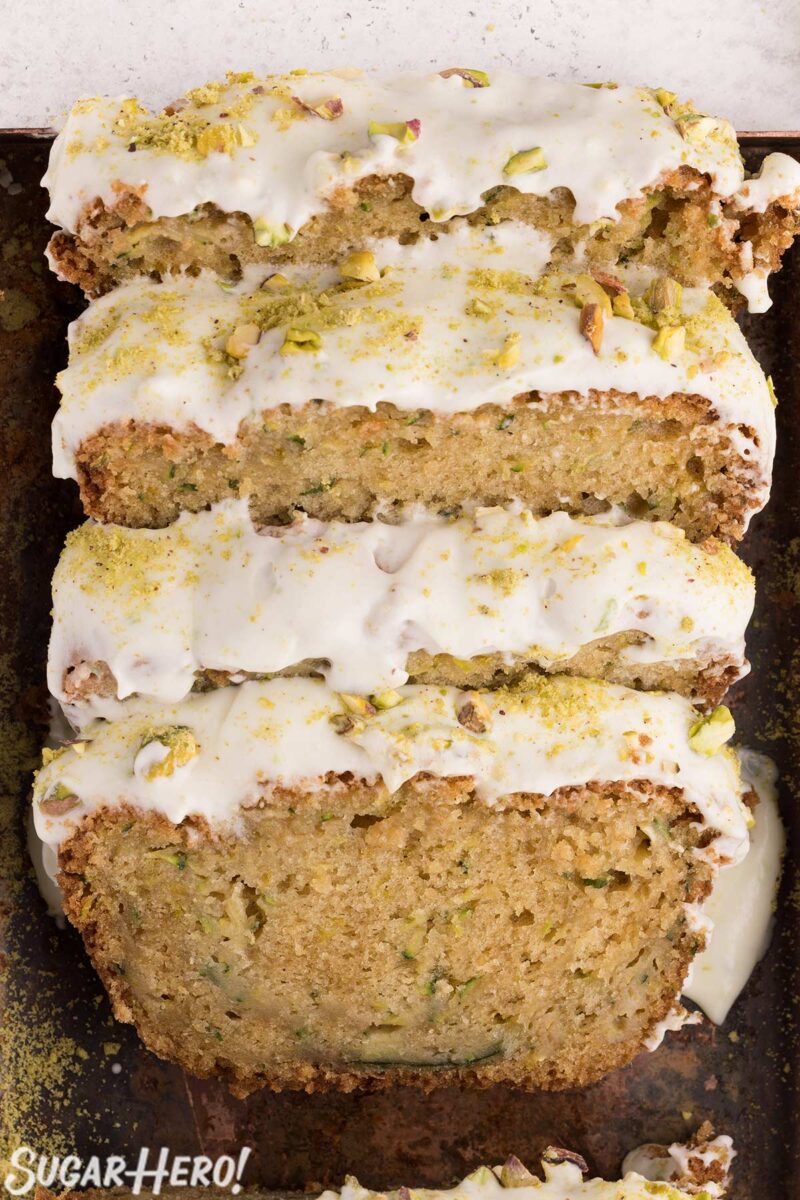 Slices of zucchini bread, with cream cheese frosting on top, resting against each other in a bread pan.