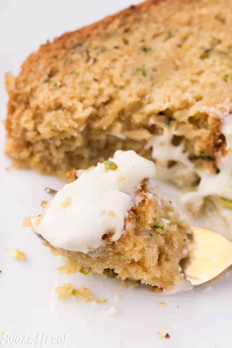 Close-up of a bite of zucchini bread, frosted with cream cheese frosting, on a gold fork.