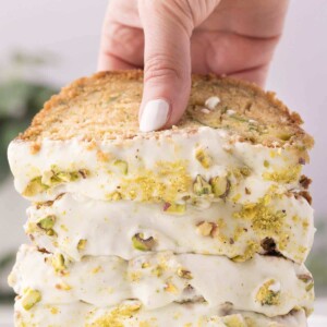 A stack of zucchini bread frosted with cream cheese frosting, with a hand lifting up the top piece of bread.