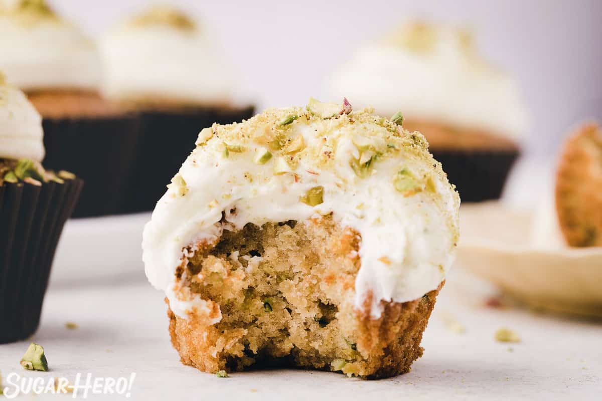 Close-up of zucchini cupcake frosted with cream cheese frosting, with a big bite taken out of it.