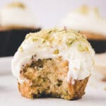 Close-up of zucchini cupcake frosted with cream cheese frosting, with a big bite taken out of it.