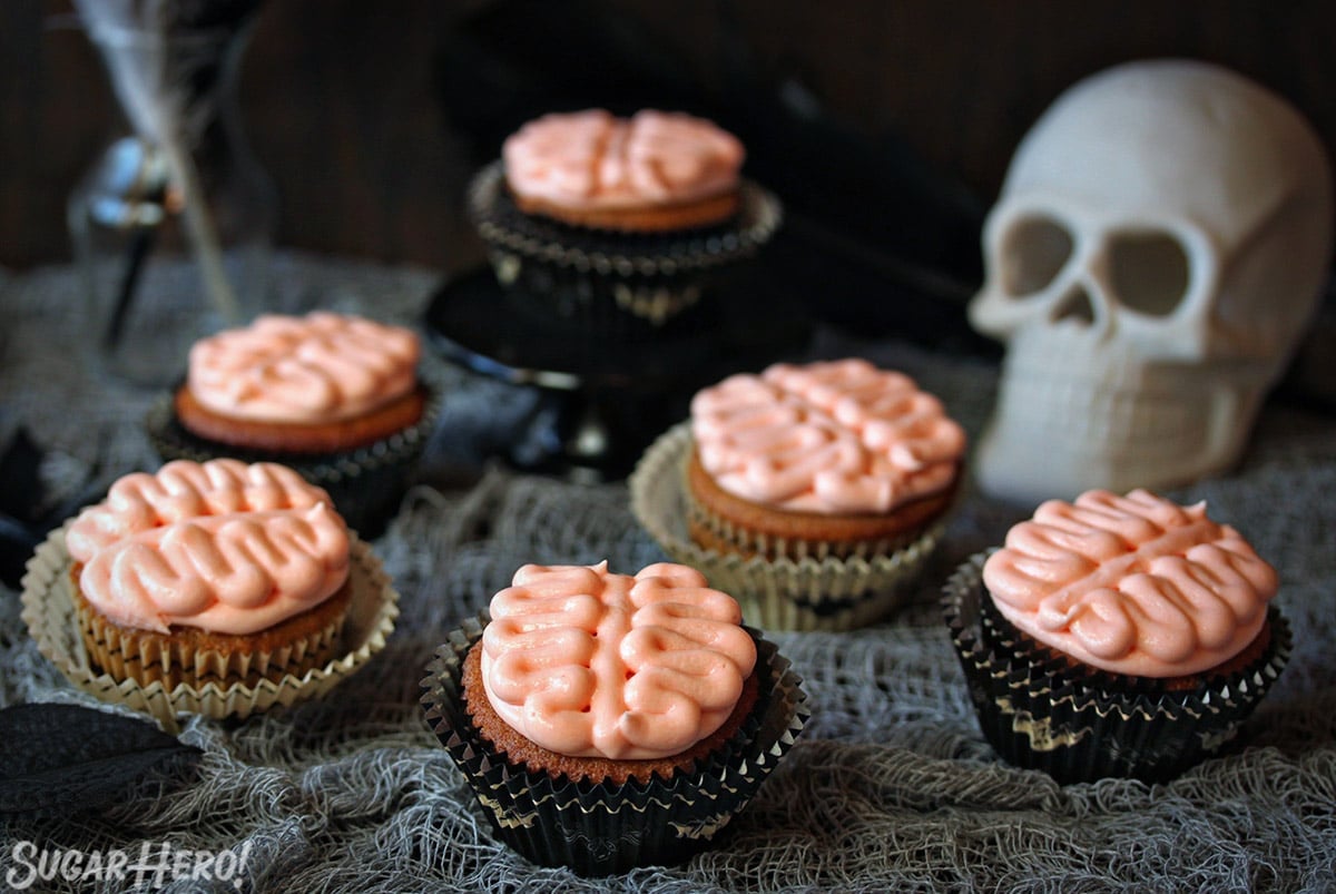 6 Brain Cupcakes next to a skull on a grey webbed tablecloth.