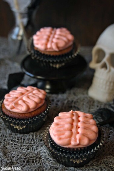 3 Brain Cupcakes next to a skull on a grey webbed tablecloth.