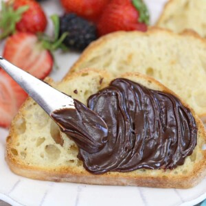 Close up of chocolate spread being swirled across the top of toast with berries in the background.