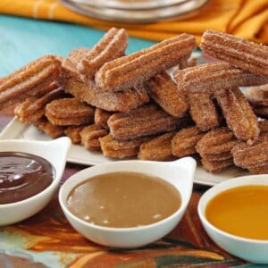 Chocolate, Dulce de Leche and Mango sauces in the foreground with a large plate of churros in the back.