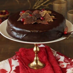 Cranberry Chocolate Truffle Cake on a white and gold cake stand sitting on red and white napkins.