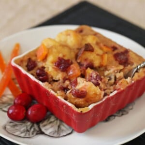 Cranberry Orange Bread Pudding in a red square baking dish next to cranberries and candied oranges.