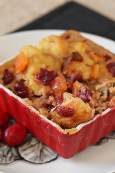 Cranberry Orange Bread Pudding in a red square baking dish next to cranberries and candied oranges.