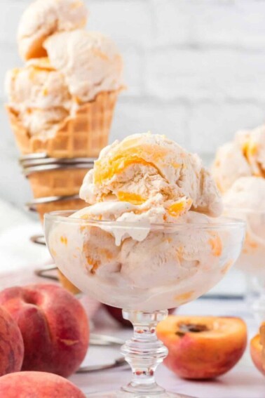 No-Churn Peach Ice Cream in a clear glass bowl and in a waffle cone with peaches in the background.