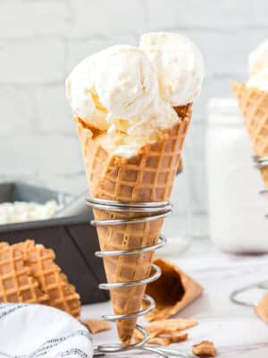 Waffle cone with scoops of vanilla ice cream, standing upright in a silver cone holder.