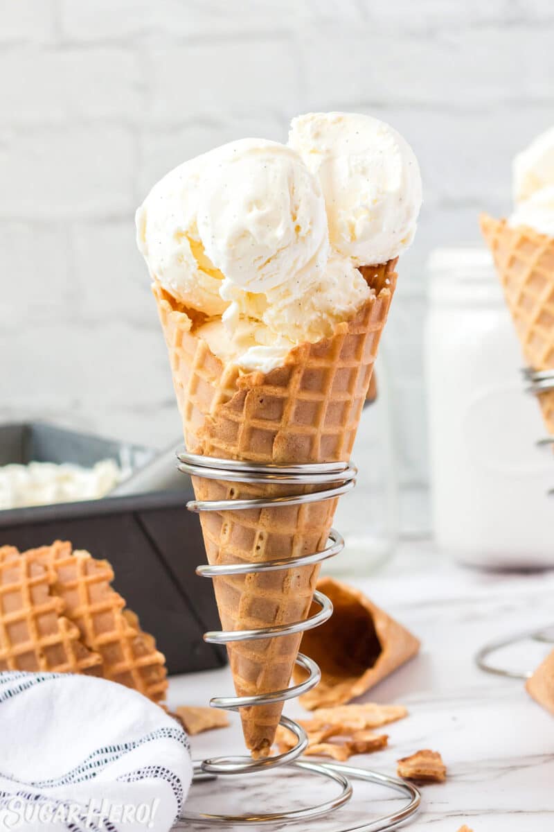 Waffle cone with scoops of vanilla ice cream, standing upright in a silver cone holder.