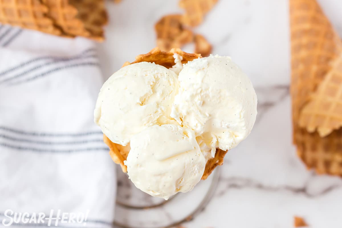 Overhead shot of waffle cone with three big scoops of vanilla ice cream inside.