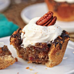 7 Mini Pecan Pies with whipped cream on top on a a white scalloped plate.