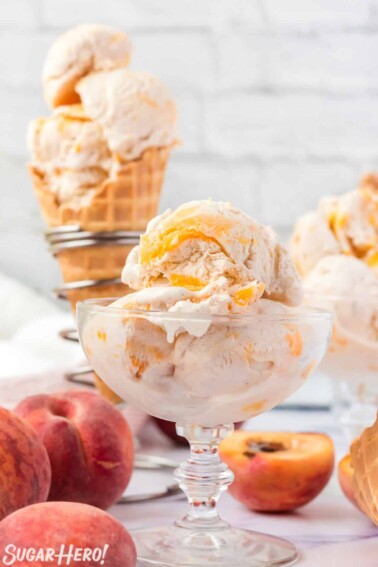 No-Churn Peach Ice Cream in a clear glass bowl and in a waffle cone with peaches in the background.