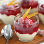 An Orange Mousse Cup with Cranberry Sauce next to 2 silver spoons on a wooden table.