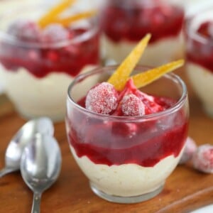 An Orange Mousse Cup with Cranberry Sauce next to 2 silver spoons on a wooden table.