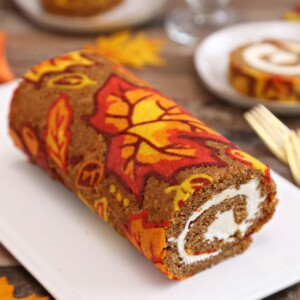 Patterned pumpkin roll on a white plate with a slice in the background.