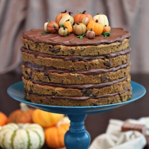 Close up of Pumpkin Chocolate Chip Cake topped with marzipan pumpkins on a blue cake stand with pumpkins in the background.