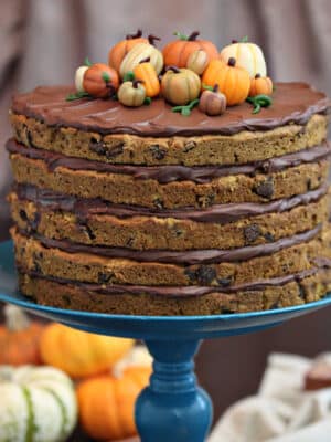 Close up of Pumpkin Chocolate Chip Cake topped with marzipan pumpkins on a blue cake stand with pumpkins in the background.