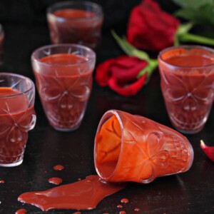 Knocked over clear skull glass of Red Velvet Hot Chocolate with 4 full glasses and 2 red roses in the background.