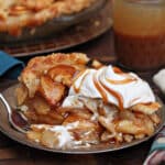 Slice of Salted Caramel Apple Pear Pie with whipped cream and caramel on top.