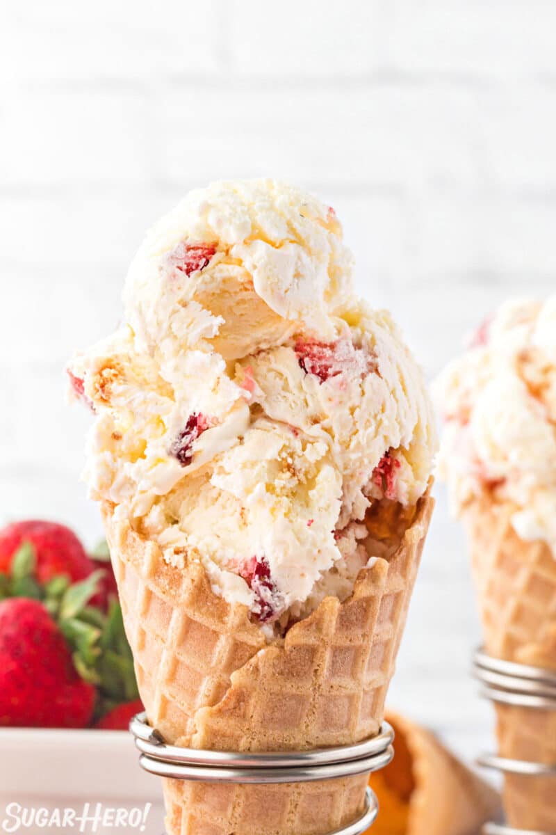 Scooped No-Churn Strawberry Shortcake Ice Cream in a waffle cone with strawberries in the background.