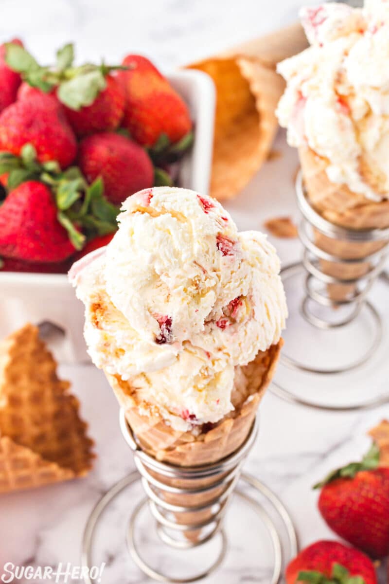 Top view of scooped No-Churn Strawberry Shortcake Ice Cream in a waffle cone with strawberries in the background.