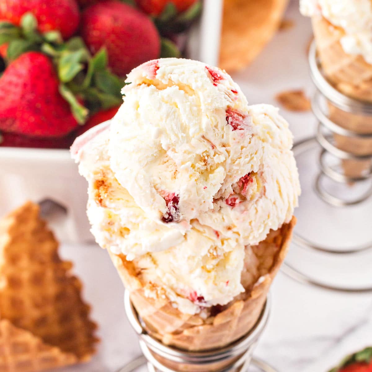 Top view of scooped No-Churn Strawberry Shortcake Ice Cream in a waffle cone with strawberries in the background.