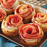 Baked Apple Cranberry Gouda Puff Pastry Roses on a baking tray on a teal napkin.