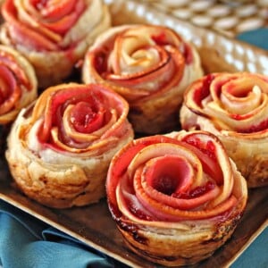 Baked Apple Cranberry Gouda Puff Pastry Roses on a baking tray on a teal napkin.