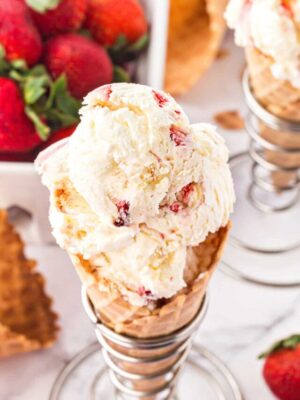 Top view of scooped No-Churn Strawberry Shortcake Ice Cream in a waffle cone with strawberries in the background.