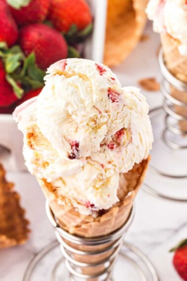 Top view of scooped No-Churn Strawberry Shortcake Ice Cream in a waffle cone with strawberries in the background.